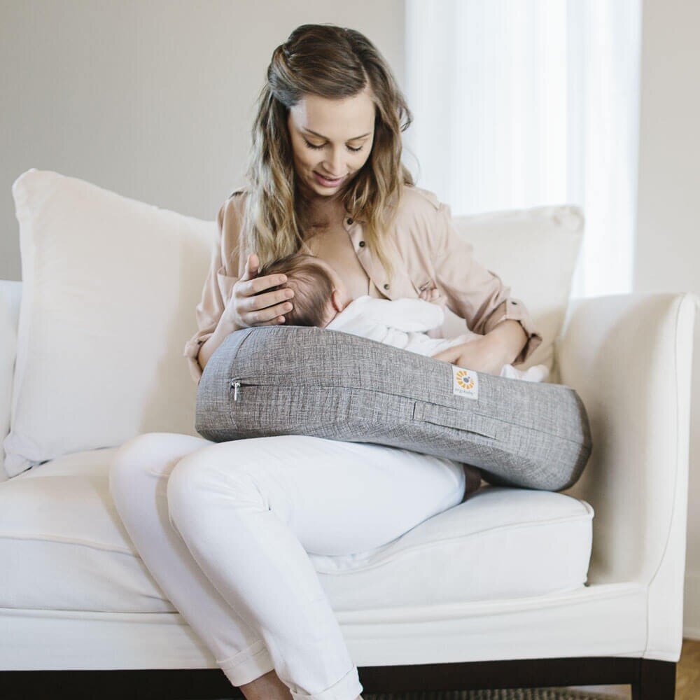 Mother nursing baby with gray nursing pillow on couch.