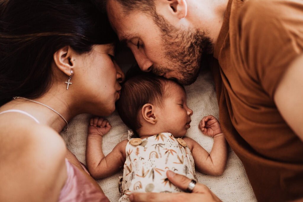Parents kissing their newborn in a family photo session.