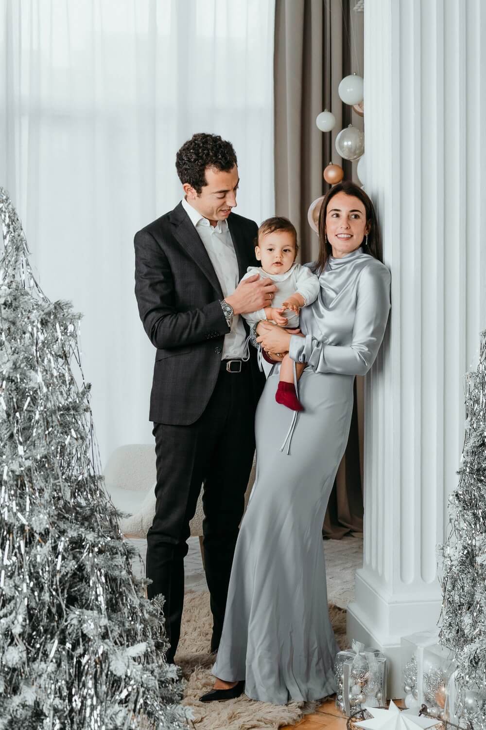 Familia sentada en el suelo abrazándose frente al árbol de Navidad.