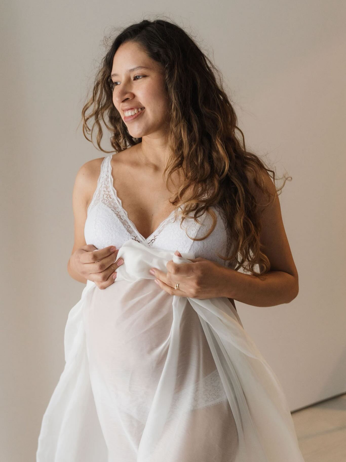 Embarazada sonriendo con tela blanca transparente en estudio, fotos embarazo cuerpo inseguridades superadas