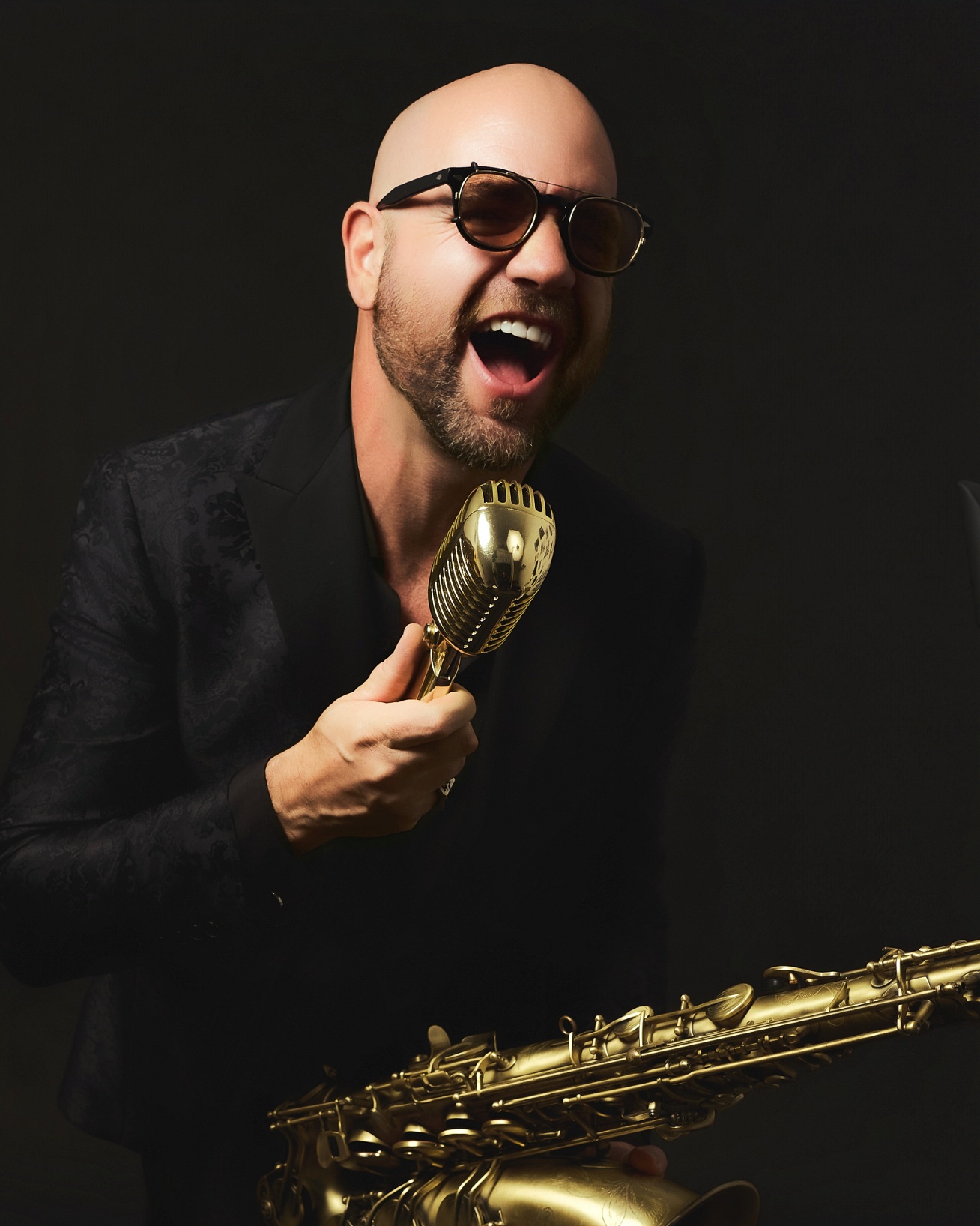 Músico con saxofón y micrófono retro posando sobre fondo negro en sesión profesional