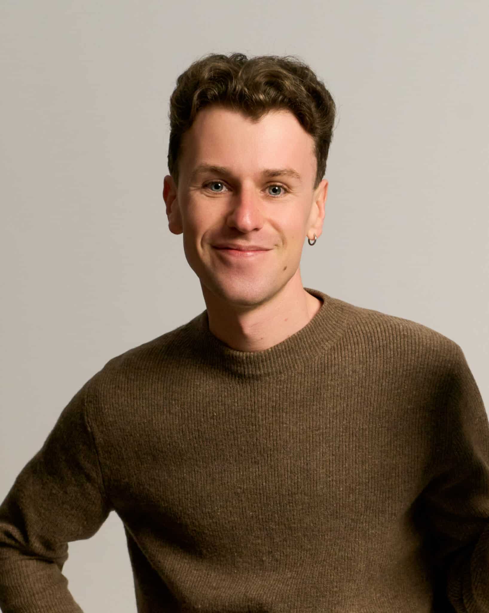 Man smiling in khaki sweater, professional studio headshot for LinkedIn