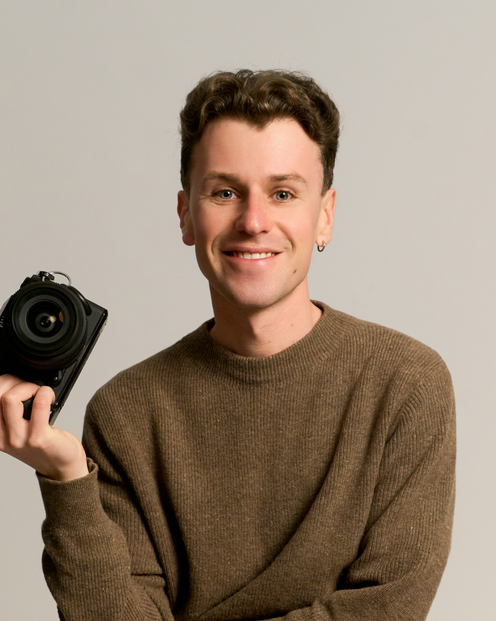 Hombre con jersey marrón y cámara en sesión de fotos profesional en estudio