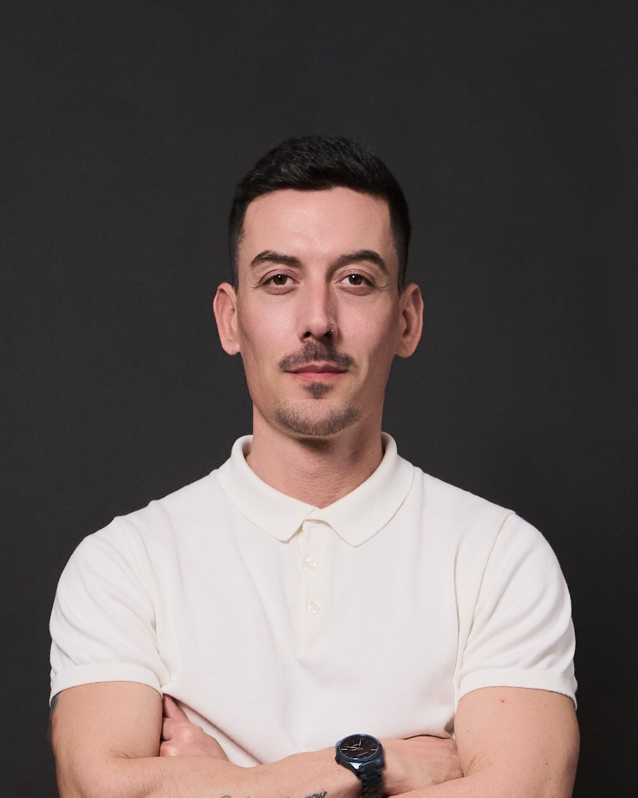 Hombre con polo blanco posando sobre fondo gris en sesión de headshot corporativo