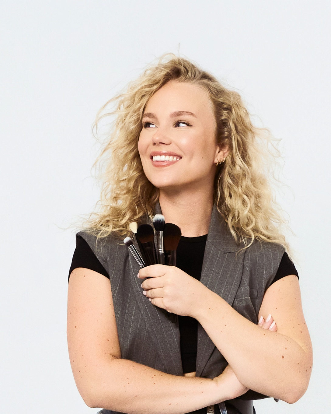 Mujer rubia con chaleco gris posando sobre fondo blanco en estudio profesional