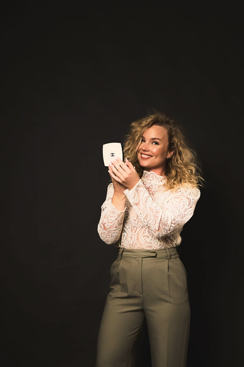 Girl looking into a small mirror during her session at YOULO, adjusting her pose with warm studio light