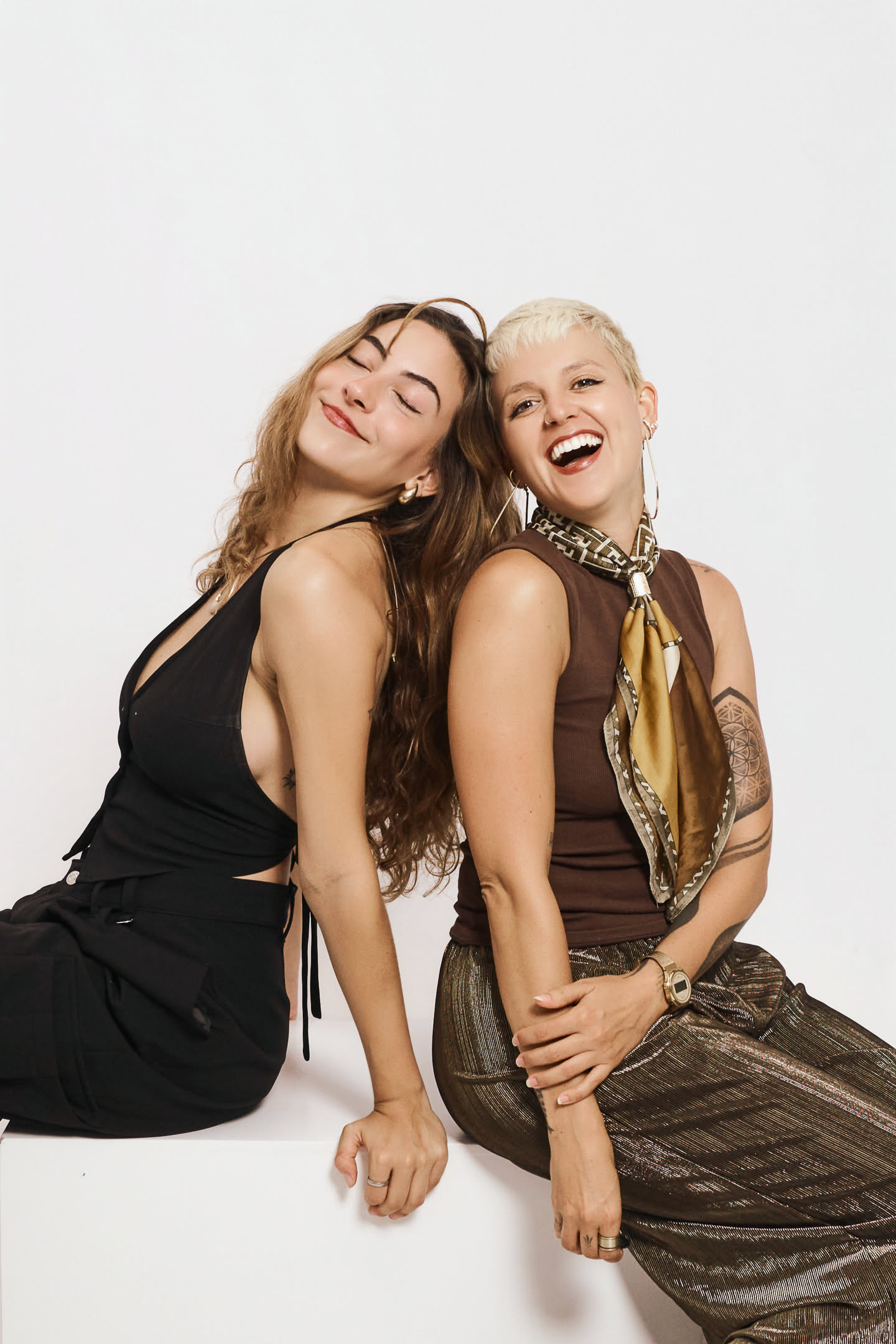 Two friends laughing back-to-back at YOULO self photo studio Barcelona, no photographer present