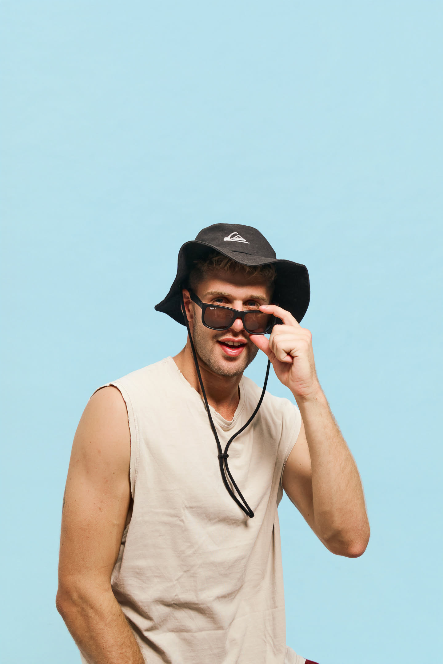 Guy with hat and sunglasses playing with props on a blue backdrop at YOULO self photo studio Barcelona