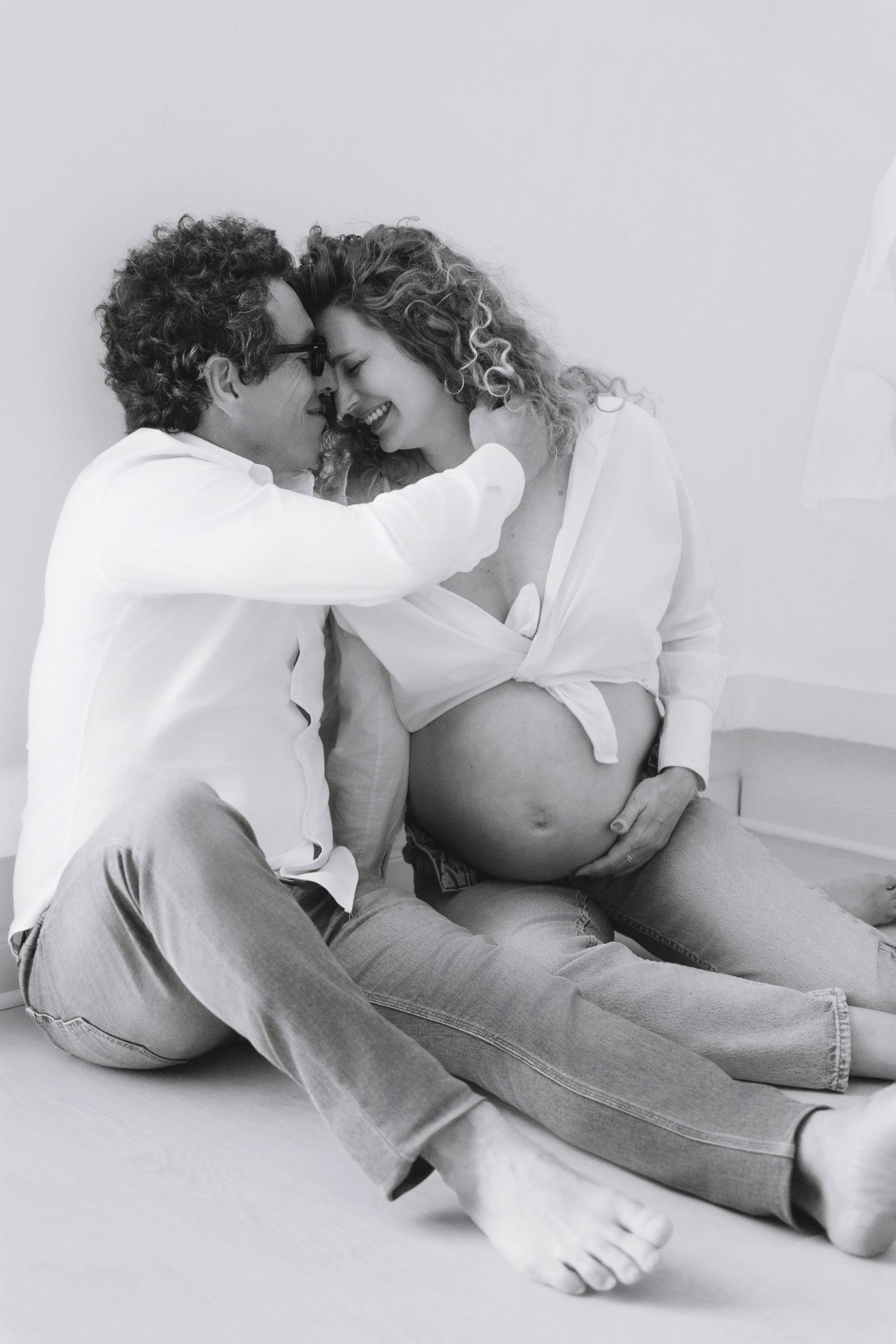 Pareja sonriendo y abrazándose en sesión de embarazo, atmósfera natural en blanco y negro en el estudio del Eixample