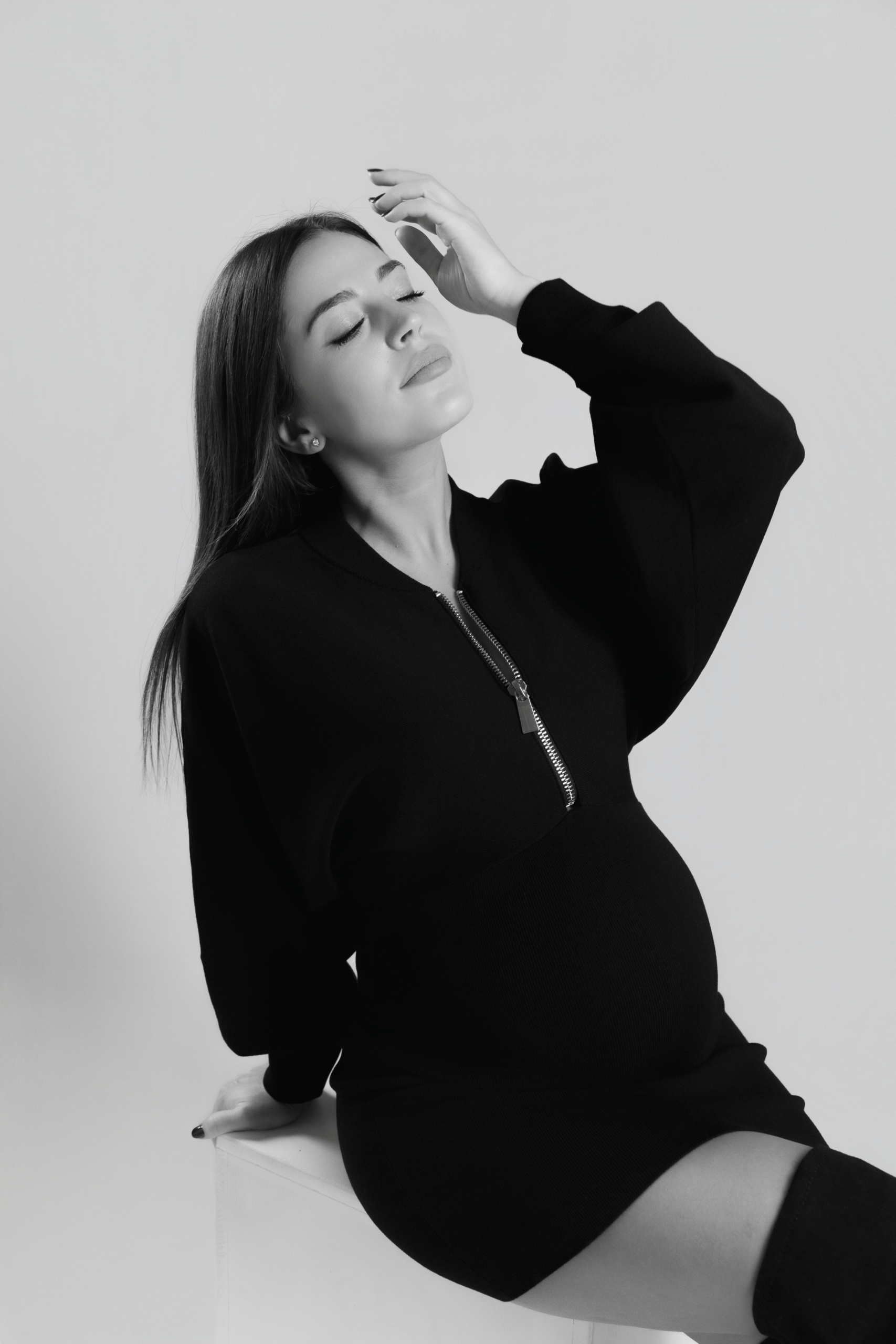 Primeriza embarazada sentada en estudio, sesión de fotos en blanco y negro, vientre marcado en semana 31 en Barcelona