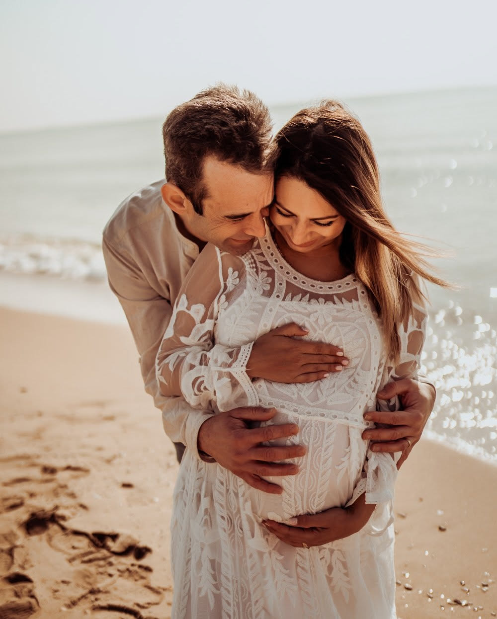 Pregnant couple at sunset on a beach near Barcelona, white dress in golden light