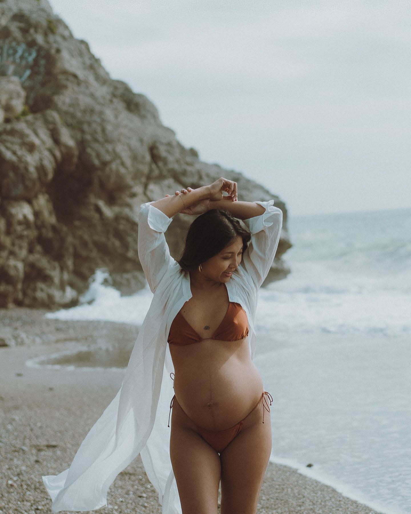 Pregnant woman in white shirt on the rocks at a cove in Sitges