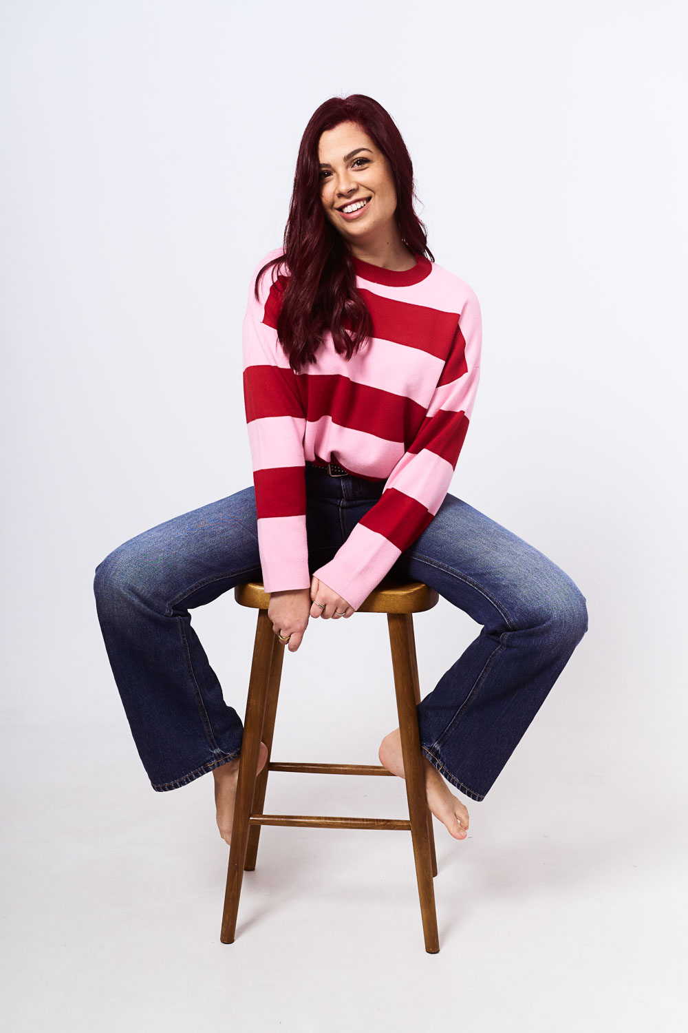 Woman sitting on a bench at YOULO Barcelona self-photo studio, pink-and-red striped jumper, white background
