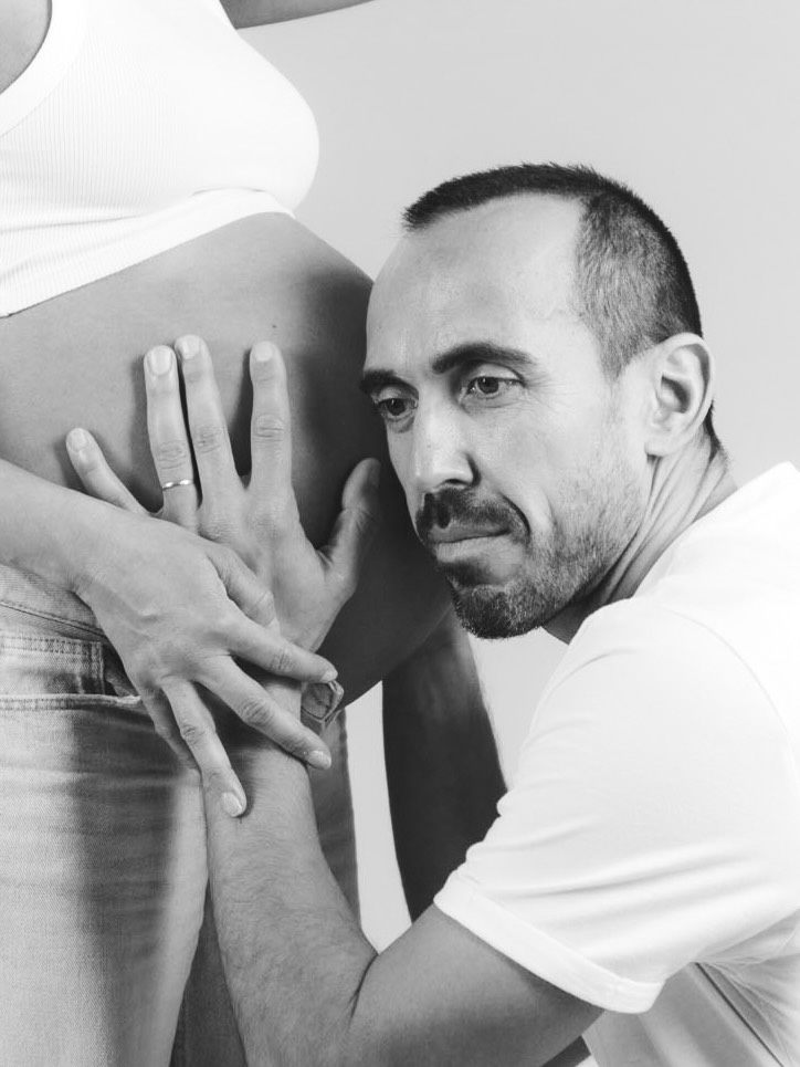 Detalle del padre apoyando manos sobre el bump con la alianza visible en sesión de fotos de embarazo