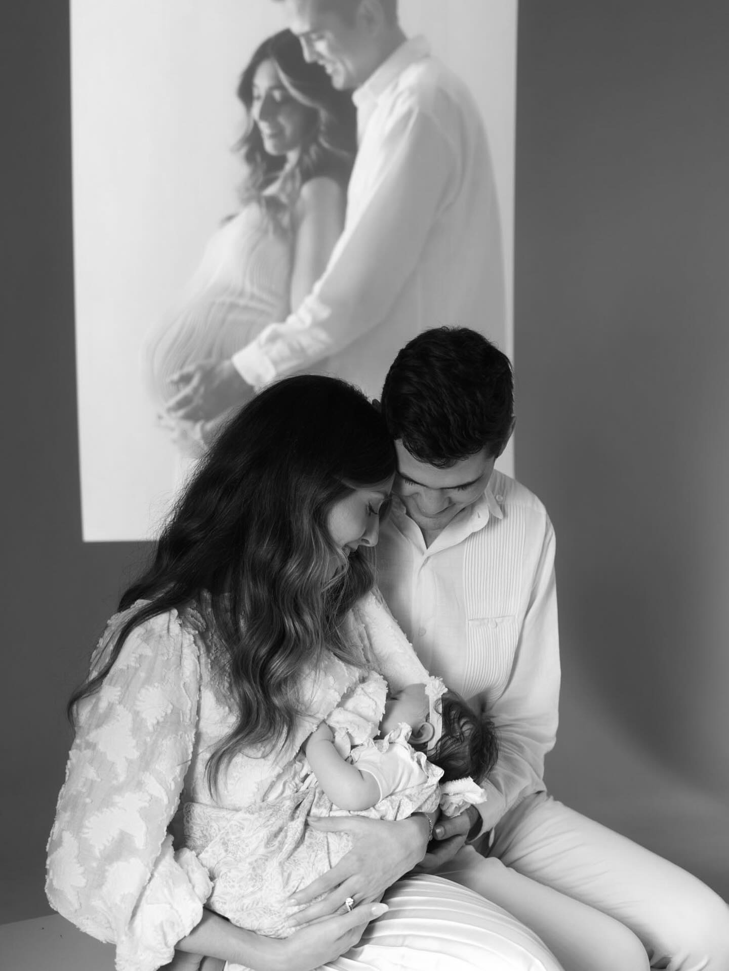 Pareja con su recién nacida en sesión de fotógrafa profesional en Barcelona, con foto de embarazo proyectada al fondo