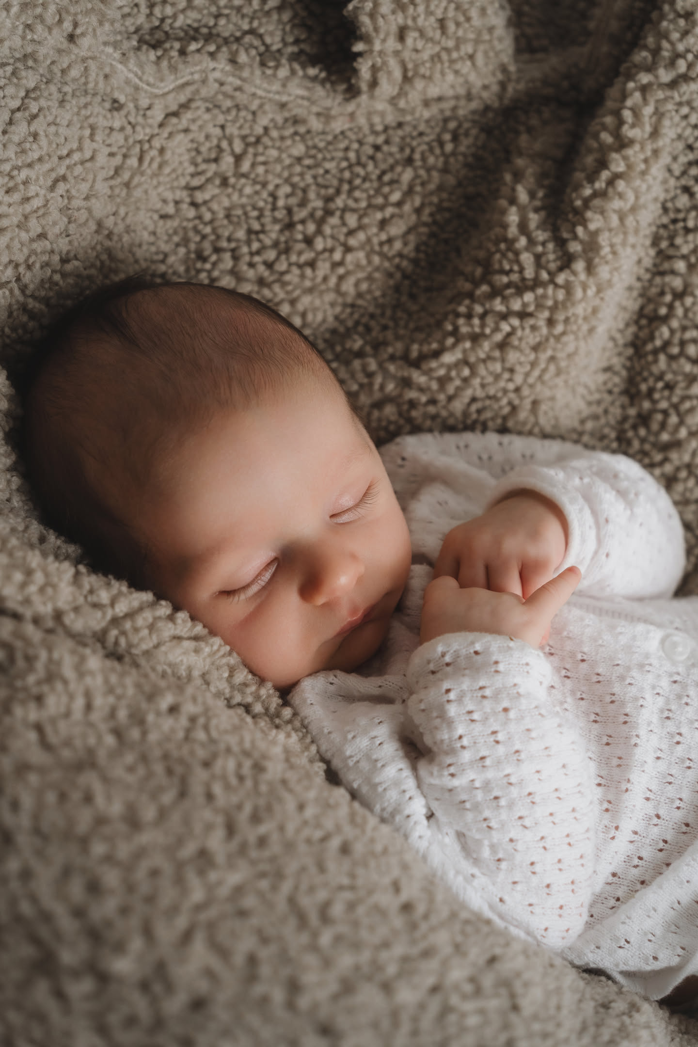 Sleeping newborn in white knit bodysuit on cream blanket in baby photoshoot