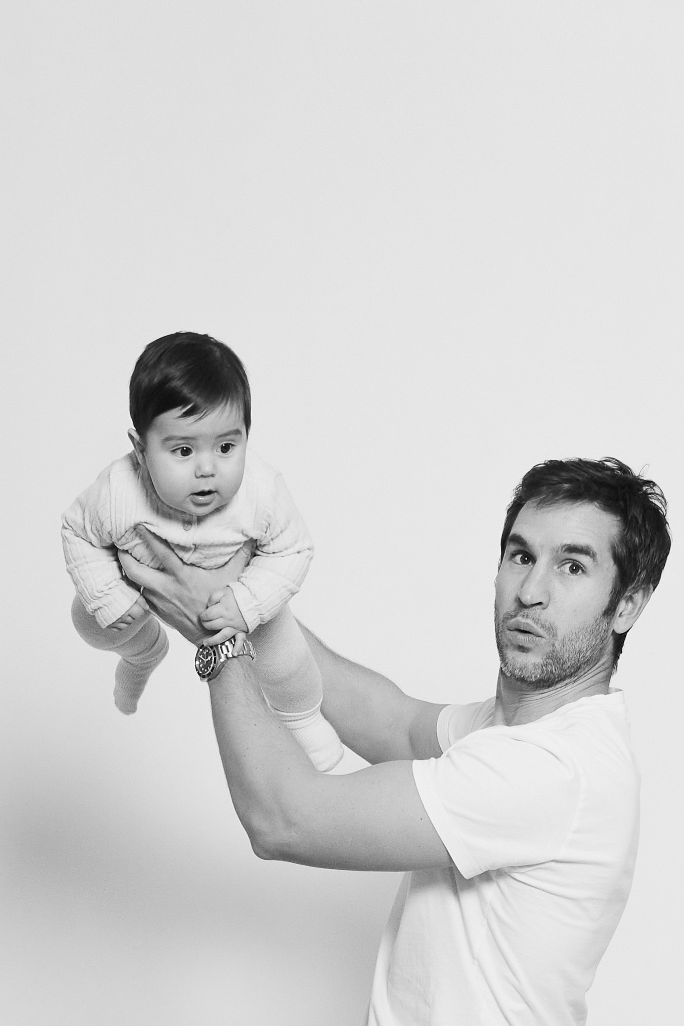 Papá levantando a su bebé durante una sesión de fotos en blanco y negro en el estudio Wonderstory de Eixample, Barcelona