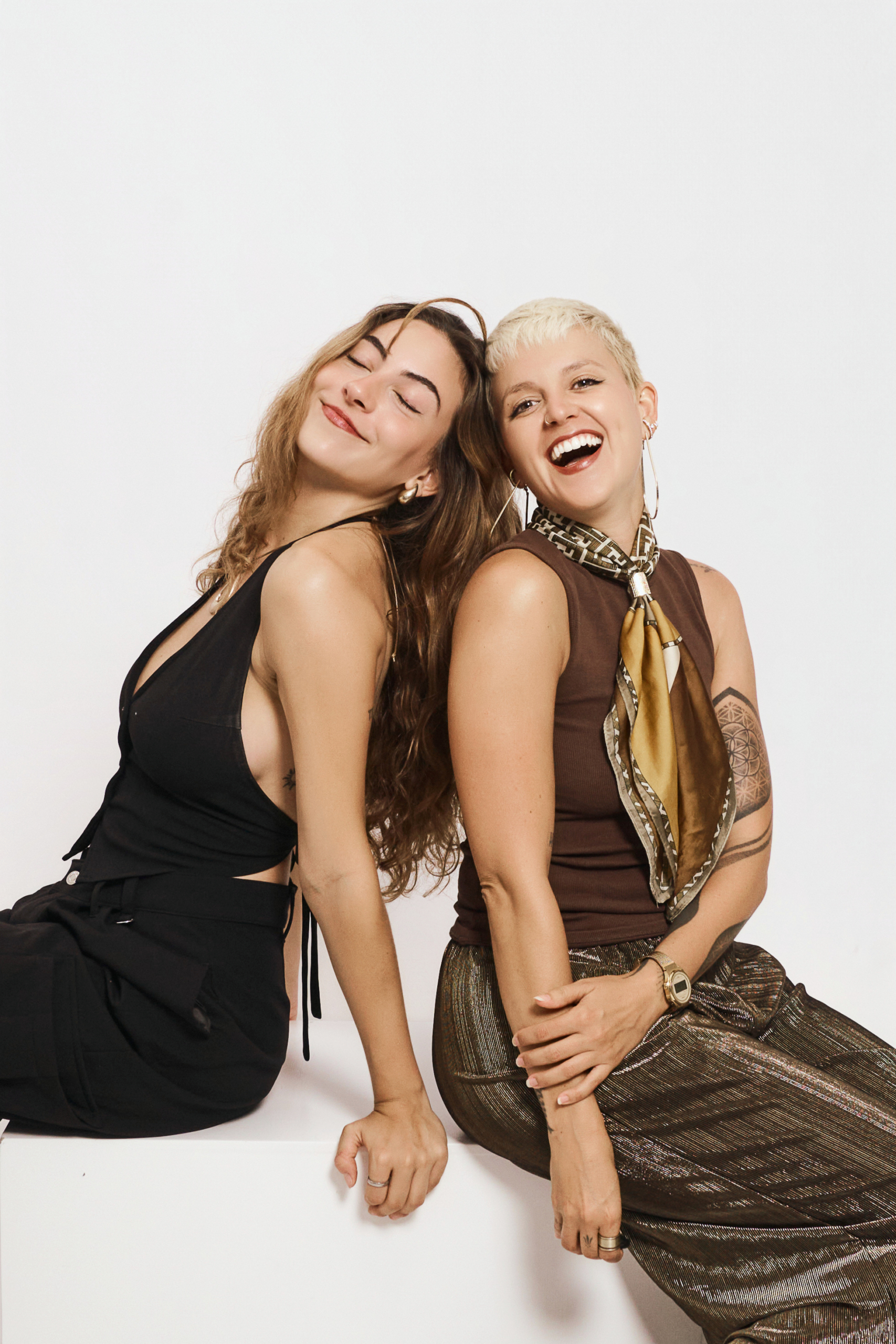 Dos amigas sentadas espalda con espalda en el suelo del estudio, riendose