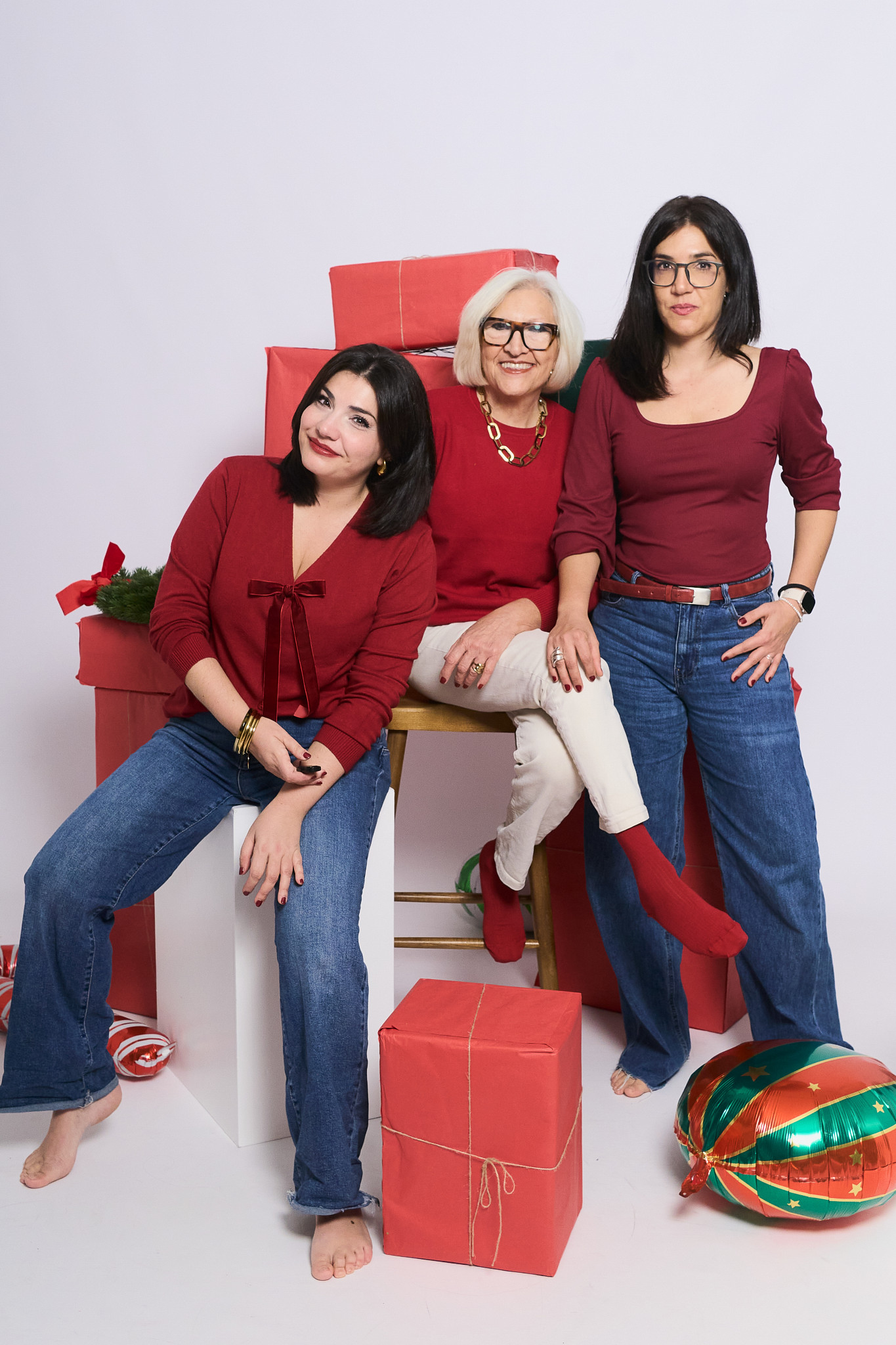 Tres generaciones de mujeres vestidas de rojo sentadas sobre cajas de regalo y bolas de Navidad