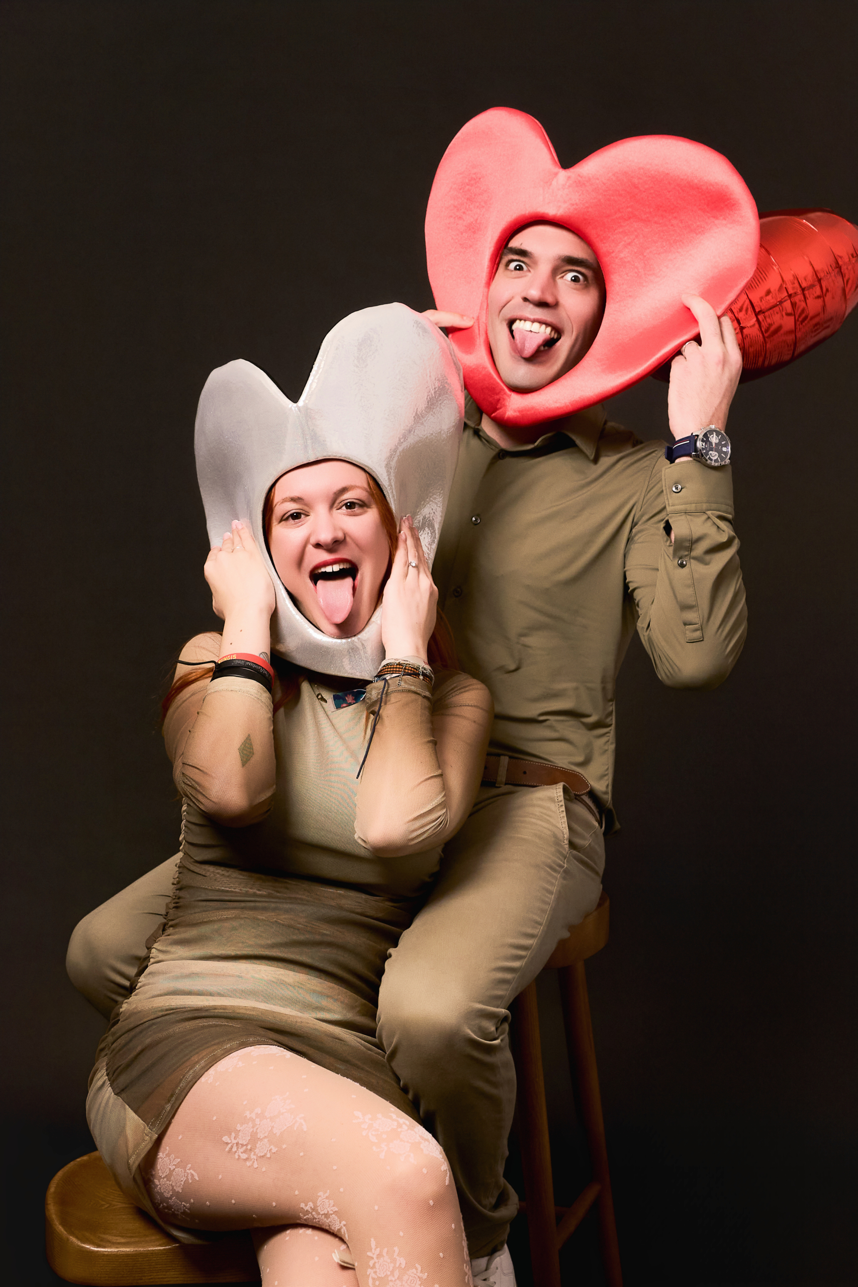 Pareja con gorros gigantes en forma de corazon sacando la lengua, haciendo el tonto
