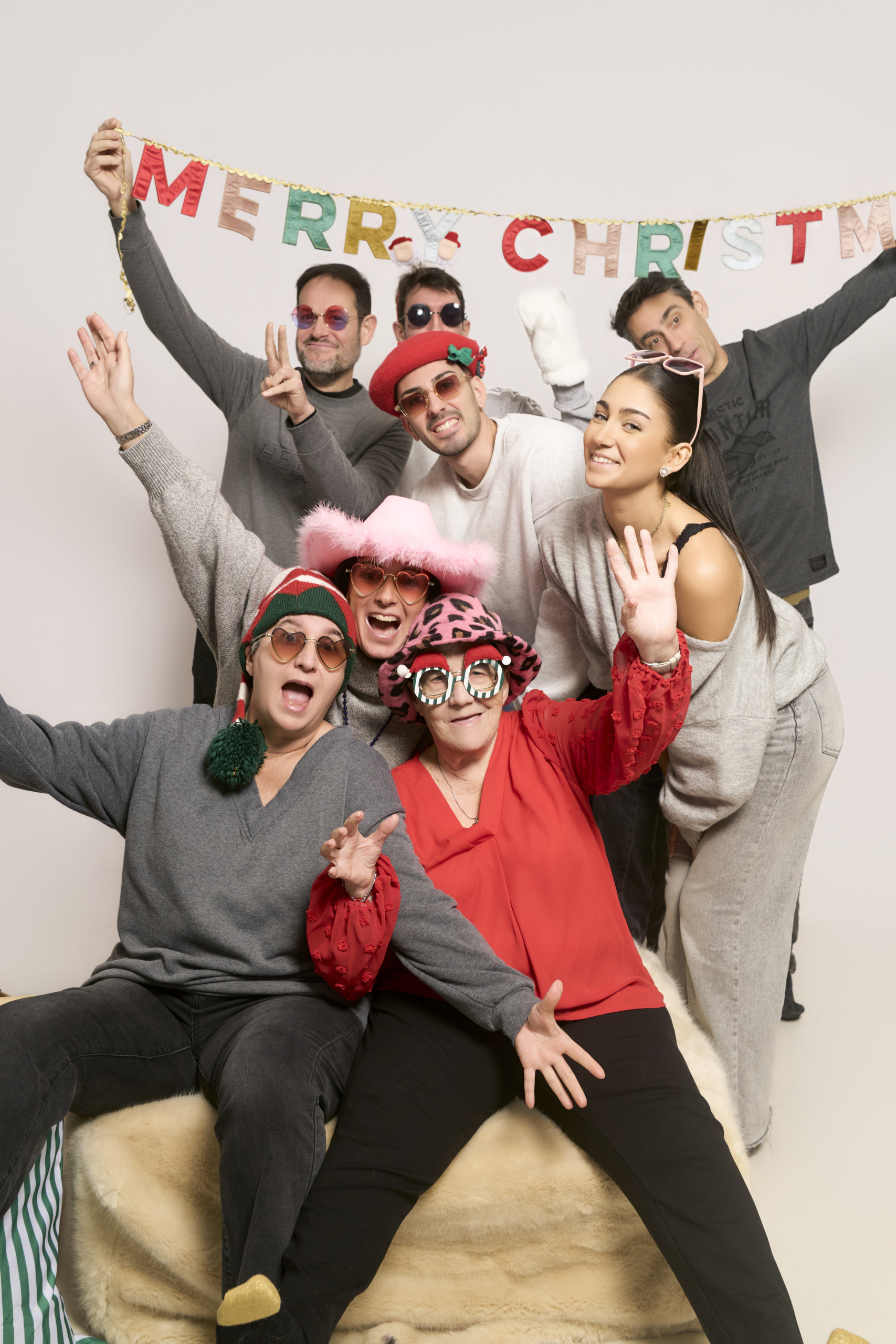 Tres generaciones haciéndose fotos solas bajo un cartel de Merry Christmas en Barcelona