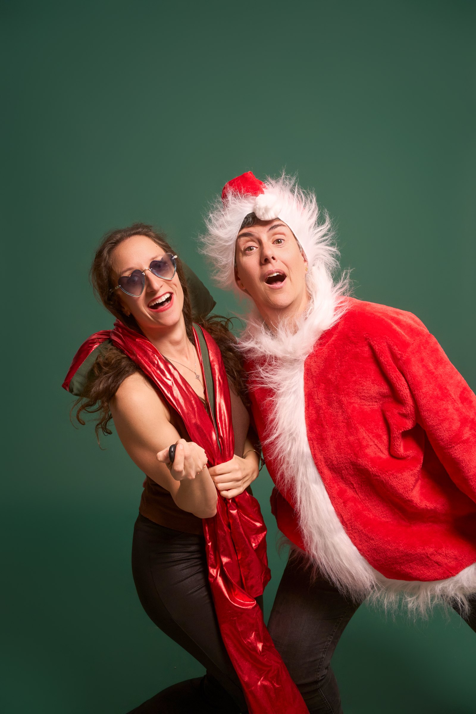 Dos amics amb jaqueta de Pare Noel i ulleres de cor a l'estudi YOULO, fons verd