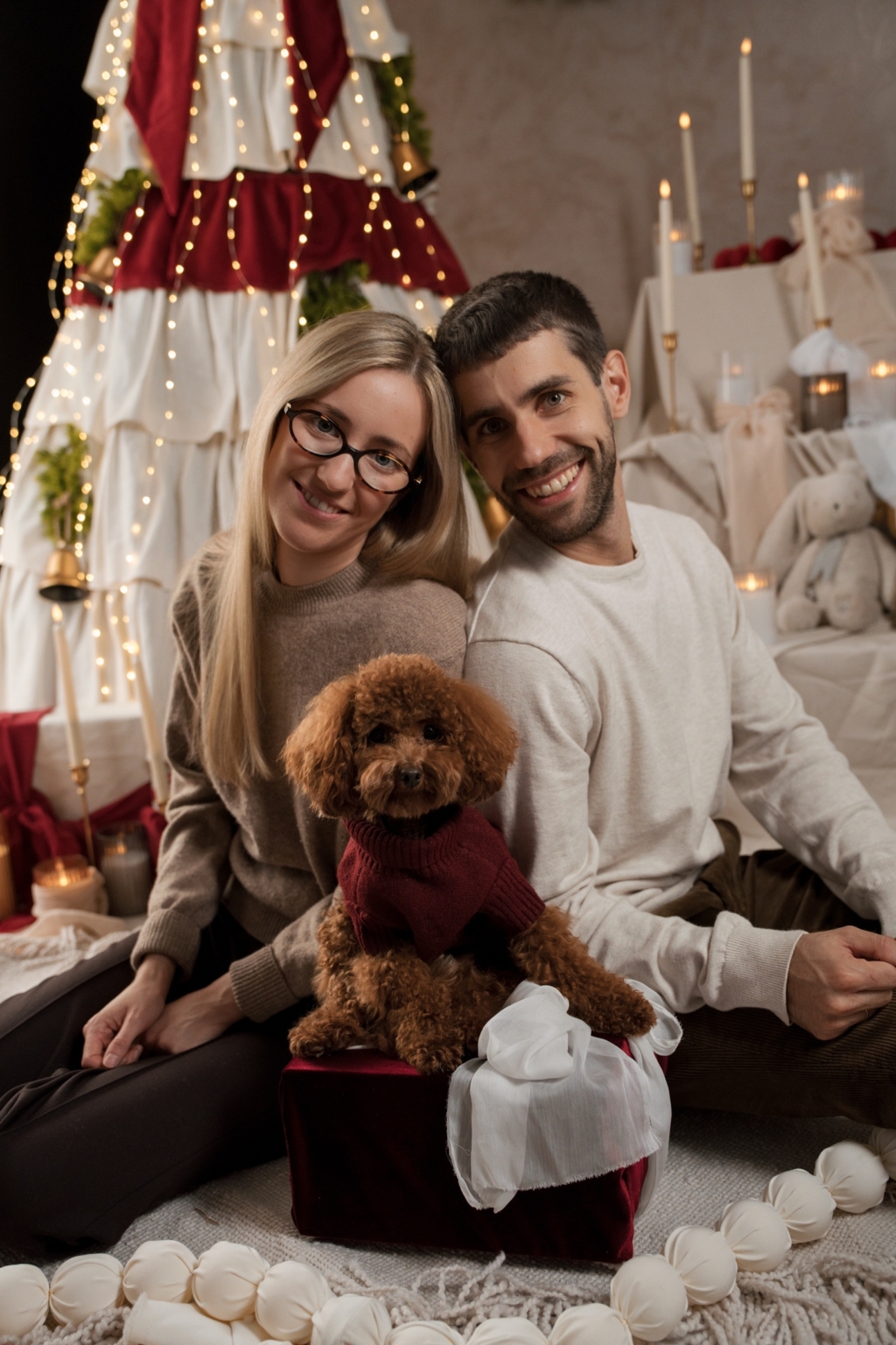 Couple with their poodle in a burgundy jumper by the ruffled tree and candles of the 2026 Christmas set